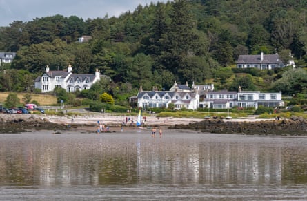 White painted houses dotted on a forested hill and people on a small beach at low tide