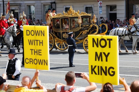 Anti-royalists holding placards as King Charles and Queen Camilla travel by carriage to the Houses of Parliament.