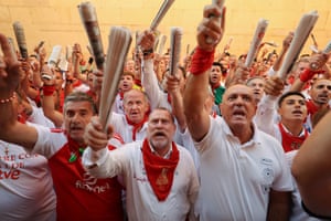 A crowd of men dressed in white with red neckties wave rolled-up newspapers as they chant