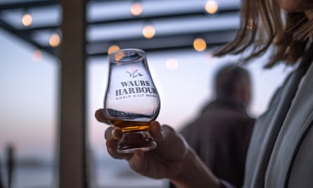 Close up of hand holding a whisky glass with Waubs Harbour branding on the front of it.