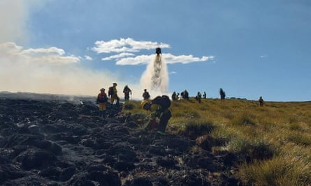 Helicopter dropping water in background as firefighters work on scorched ground