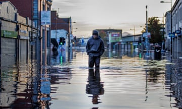 A man walks through knee-high flood water on a shopping street