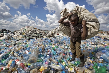 A waste collector carries a sack of plastic bottles to be sold for recycling.