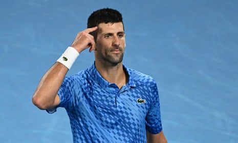 Novak Djokovic points his finger to his head in celebration.