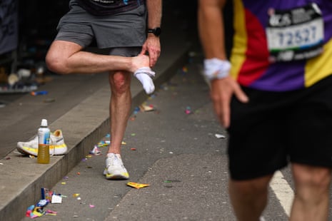 A runner takes off a shoe and sock and checks his feet as he takes a brief break from the London Marathon 2025