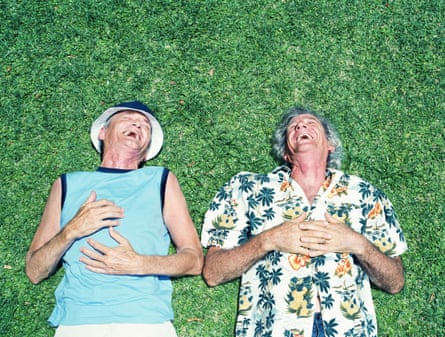 Two older men lying on their backs on grass, laughing, overhead view.