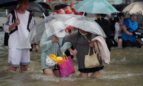 Residents, holding umbrellas amid heavy rainfall, wade through floodwaters on a road in Zhengzhou, Henan