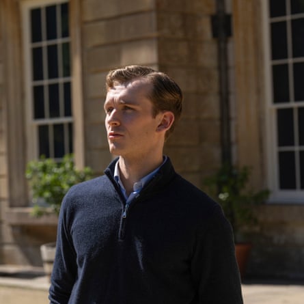 HARRY LAWTEY as the character Robert Spearing in the TV drama Industry, standing outside a large house wearing a navy quarter-zip sweater.