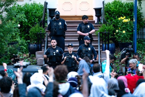 uniformed police stand on stairs in front of crowd of people