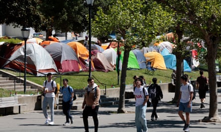 Students walk by dozens of colorful tents on a green lawn.