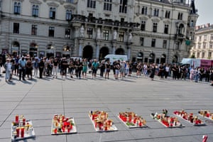 A crowd of people stand in front of tributes laid out in the main square
