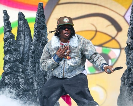 A man standing on stage holding a microphone with props and a colourful background behind him