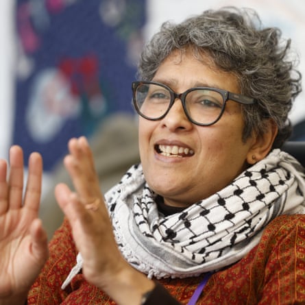 Dania Thomas, with short wavy hair, glasses and a cloth scarf, holds up her hands and talks, smiling