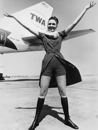 A flight attendant stands beside a TWA plane with her hands in the air