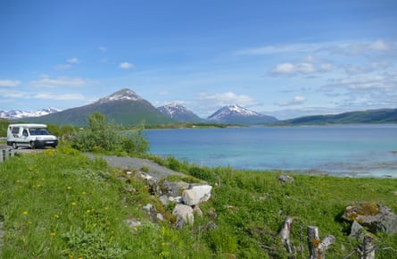 A campervan by a lake with mountains and blue skies behind