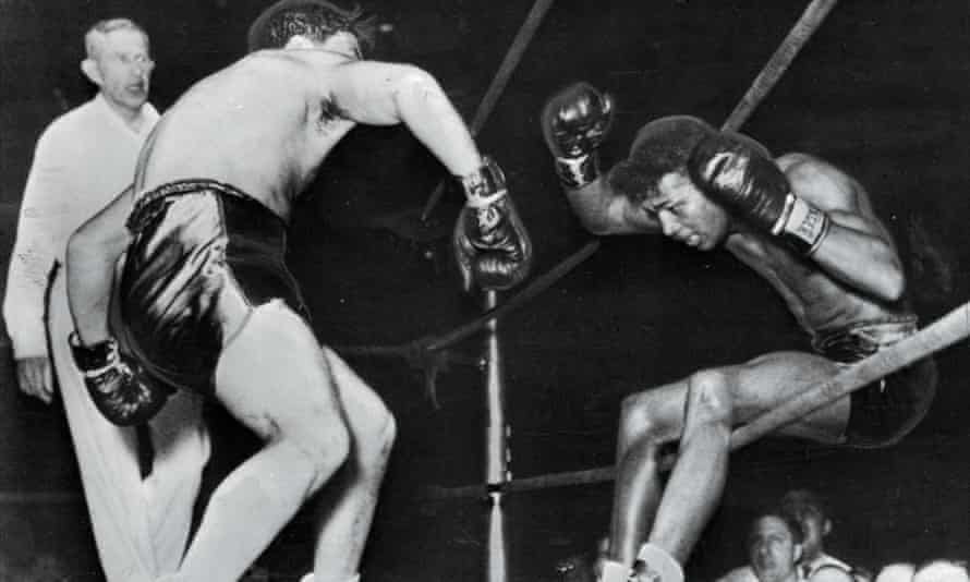 Sugar Ray Robinson falls through the ropes of a Detroit ring under the impact of Jake LaMotta’s fists in 1943.