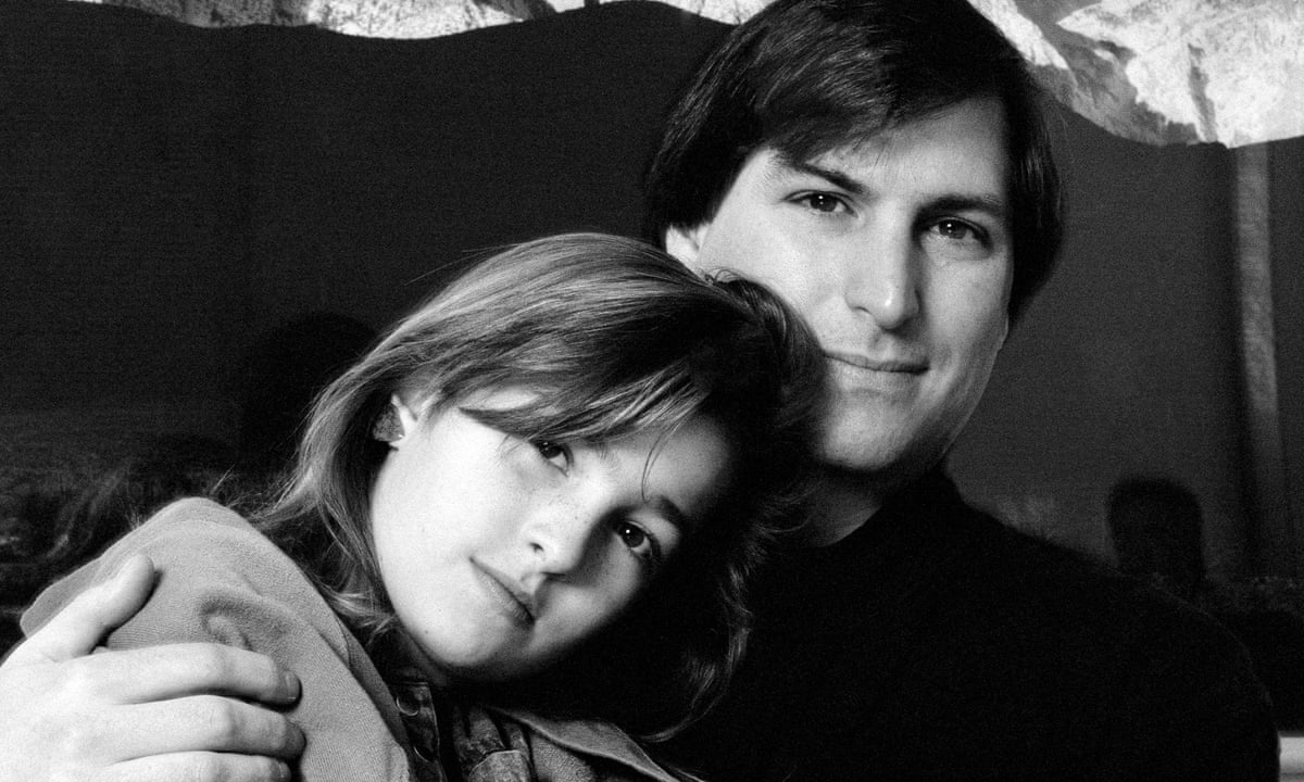 A close-up black-and-white portrait of a young Steve Jobs with his daughter, Lisa Brennan-Jobs. Lisa rests her head on her father's shoulder while he wraps an arm around her, both looking directly into the camera with soft, contemplative expressions.