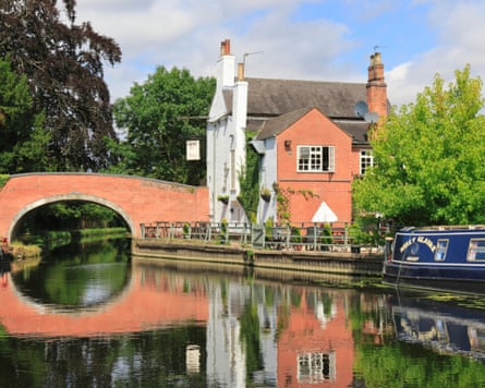 A riverside pub next to an old red brick bridge with a narrowboat moored up outside.
