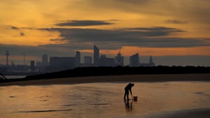 A fisherman digs for bait on a beach in front of the Liverpool skyline