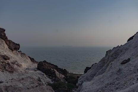 Rocky white cliffs at the strait of Hormuz frame a hazy sea with a distant ship
