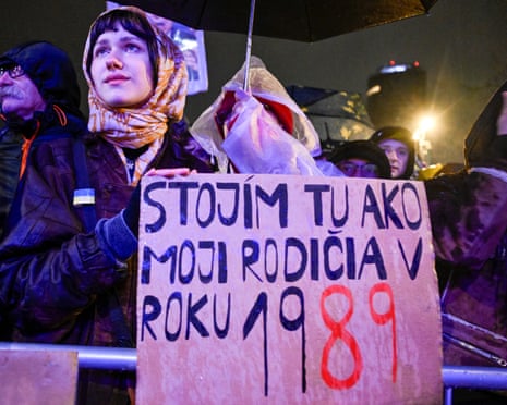 A woman holds a banner during an anti-government protest marking the 36th anniversary of the 1989 Velvet Revolution in Bratislava, Slovakia. The banner reads: "I am standing here like my parents in 1989".