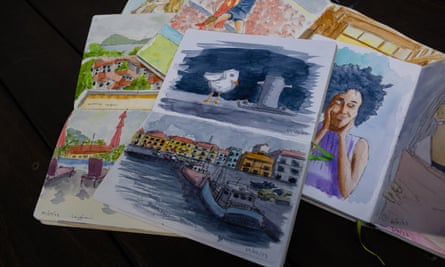 A sketchbook sits on top of a pile of other sketchbooks, with a seagull painted on one page and boards in a harbour on another