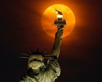 A red moon rises through a haze behind the Statue of Liberty in New York City. The author is renouncing their US citizenship