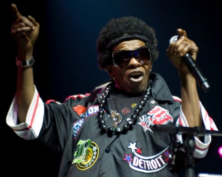 Sly Stone on stage, pointing to the sky and holding his microphone