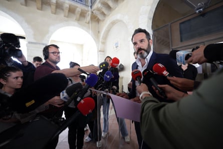 Francois Roujou de Boubée speaks to journalists, who hold microphones towards him, in a grand public building with white arches. He has short dark hair and a neat, greying beard.