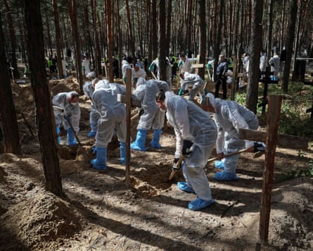 People in white overalls working to exhume bodies in a forest area