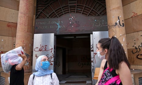 People wearing face masks stand outside the damaged entrance of the Association of Banks in Beirut.