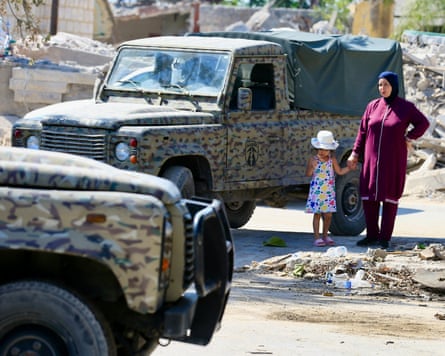 A woman and child stand next to Lebanese military vehicles