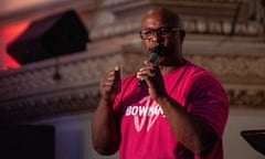 a Black man in a red shirt speaks into a microphone