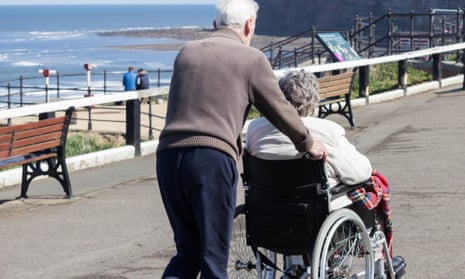 Man pushing woman in wheelchair on a path next to a beach
