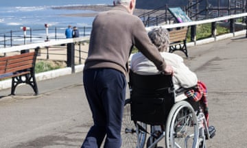 Man pushes woman in wheelchair on path next to a beach