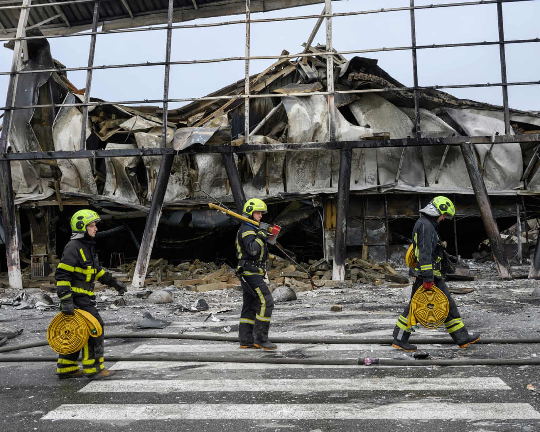 Rescuers carrying hose reels walk past a missile-damaged shopping centre in Kyiv