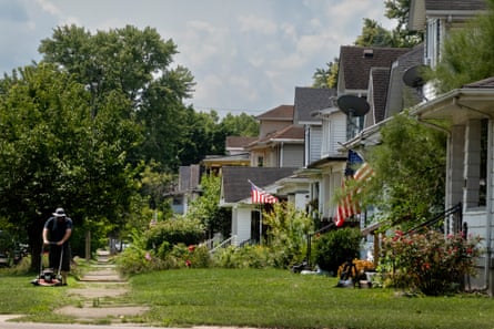 A man mows a green strip of lawn next to a line of houses, some with American flags out front, in Middletown, Ohio.