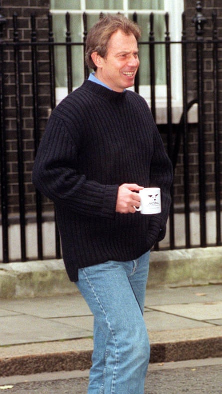 Tony Blair holds a National Canine Defence League mug as he stands smiling in the street wearing jeans and a navy jumper