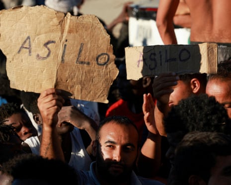 Migrants hold signs reading "asylum" in Spanish while waiting in line to receive food and beverage from the Red Cross, following mass crossings of migrants on foot and by sea from Morocco into Spanish territory, in Ceuta, Spain.