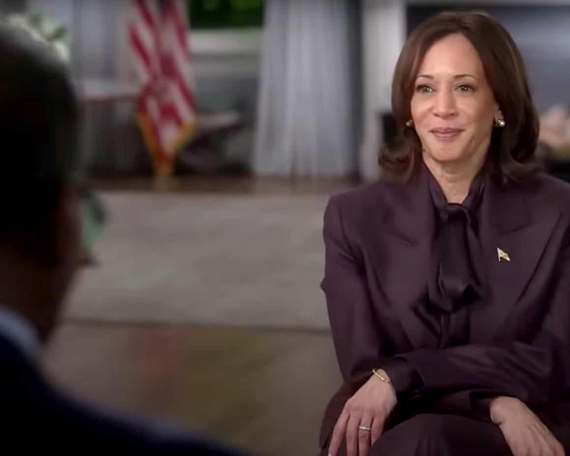 Kamala Harris crosses her hands on her knees during an interview in a room with the US flag in the background