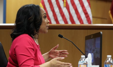 Black woman in pink speaking into a microphone in a court room