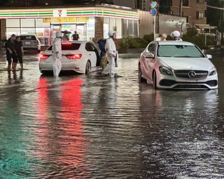 People in protective gear walk on a road where the water is up to their ankles