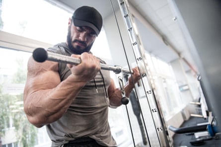 A man working out in a gym lifting heavy weights and looking at his arm muscles