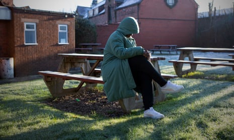 A woman wearing a hooded jacket sitting alone on a bench