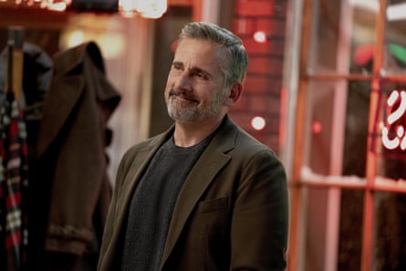A smiling man with beard wearing a brown jacket and black T-shirt leaning slightly backwards