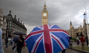 A pedestrian shelters from the rain beneath a union flag umbrella near the Houses of Parliament in London.