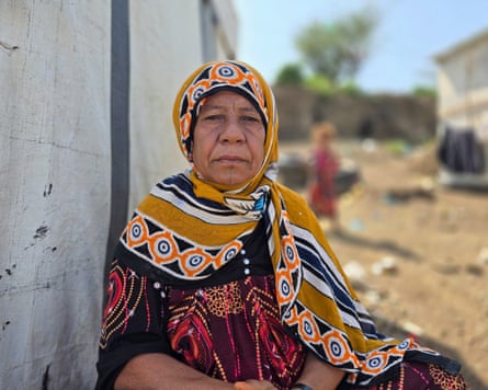 Asma Taleb, wearing a yellow patterned hijab and a red patterned dress, poses unsmiling, looking at the camera
