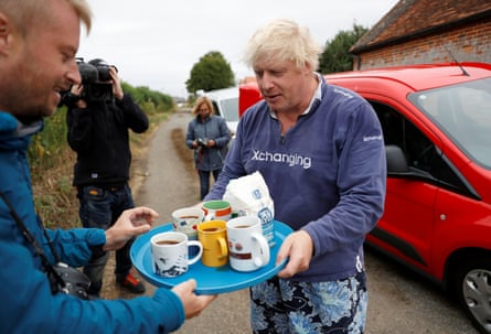 Boris Johnson carries a tray of mugs which he is giving to journalists outside his home