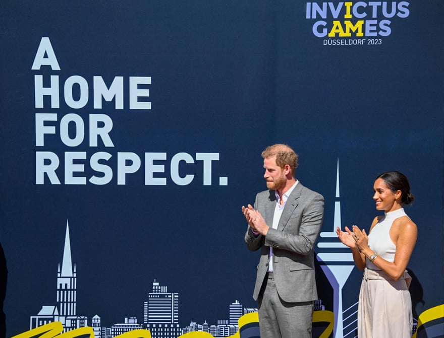 The Duke and Duchess of Sussex stand together in front of a backdrop for the Invictus Games.