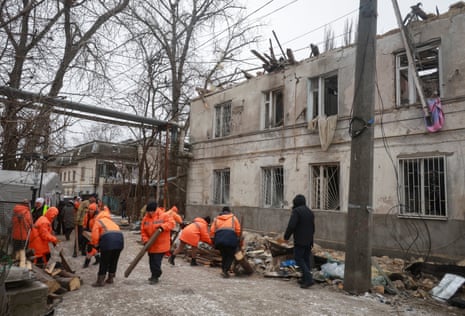 People dressed in orange hi-vis jackets clean up the debris on a street affected by the drone strike